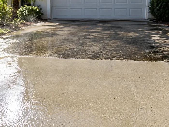 Concrete driveway half cleaned, algae staining on one side and clean slab on the other